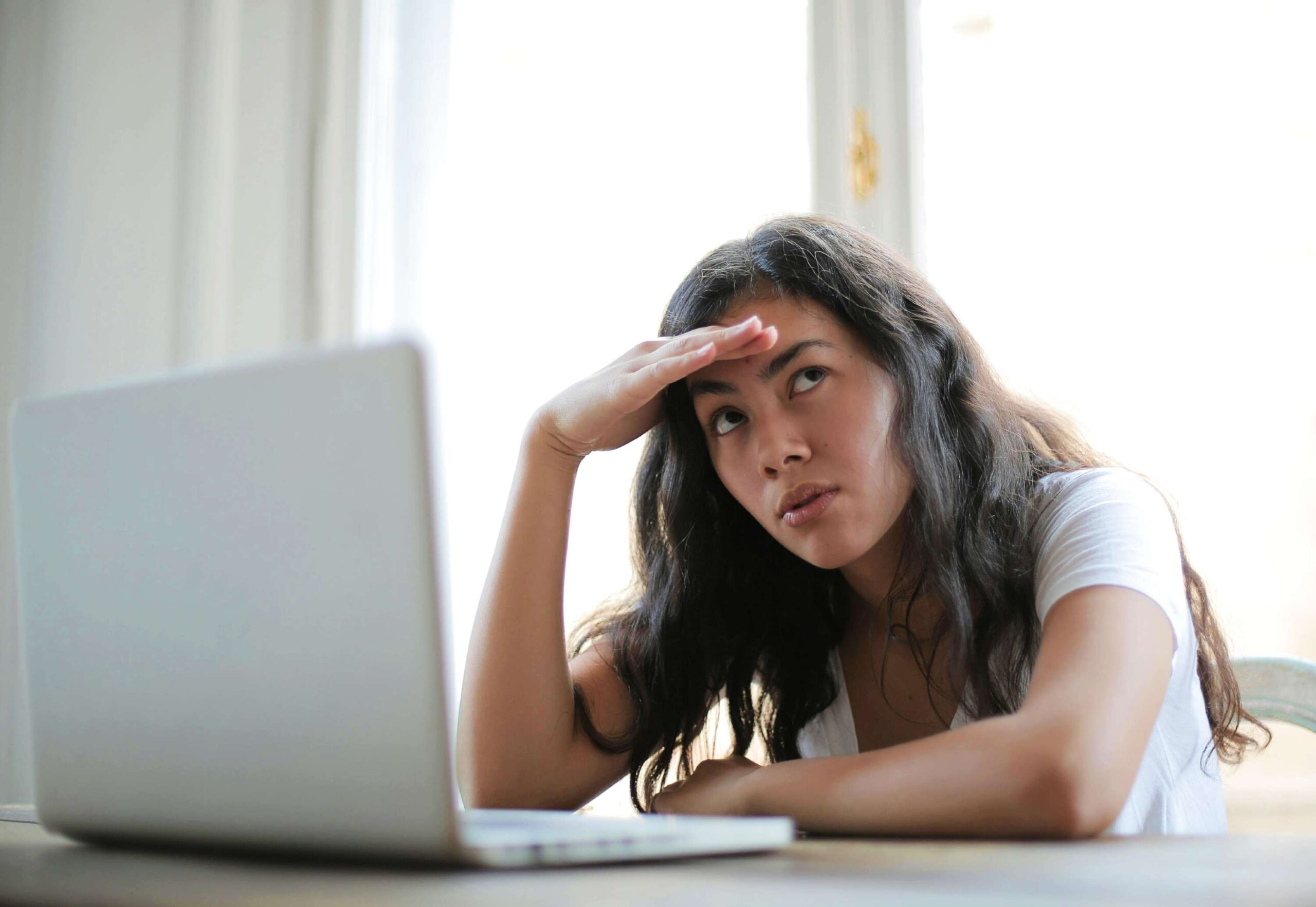 A young girl with a puzzled expression sitting in front of her laptop.