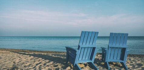 Two sun lounger chairs facing towards the shore of a beach.