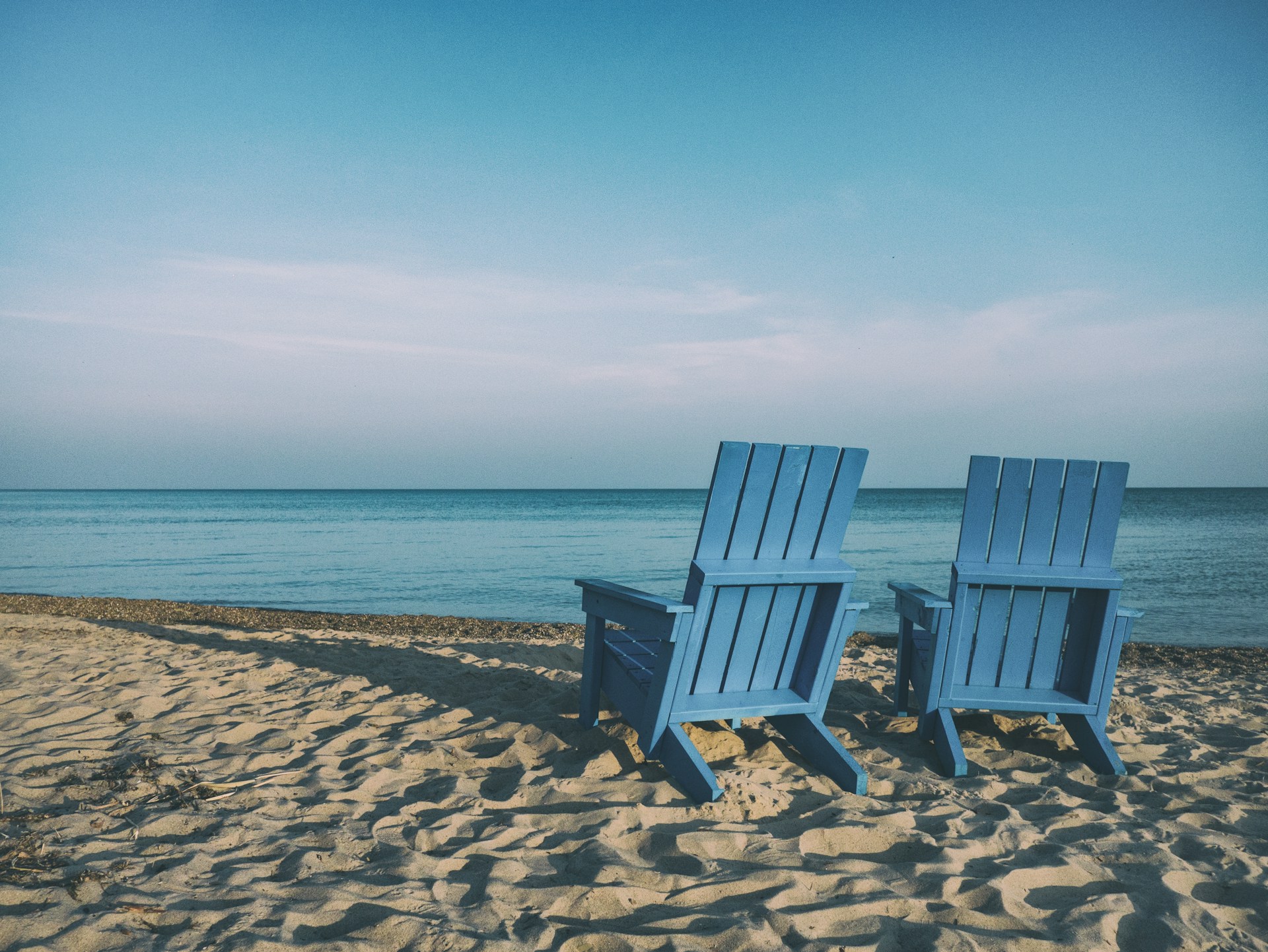 Two sun lounger chairs facing towards the shore of a beach.