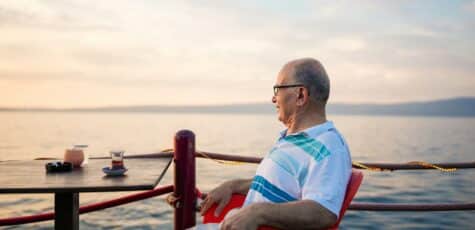 A man in his 50s sitting next to a body of water, contemplating saving for retirement.